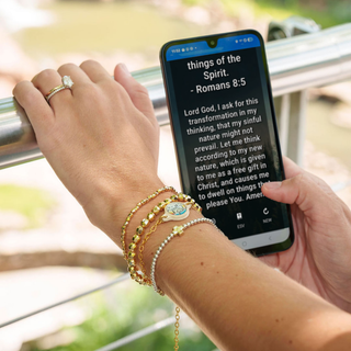 Person holding a phone with a Bible verse displayed, wearing multiple bracelets.