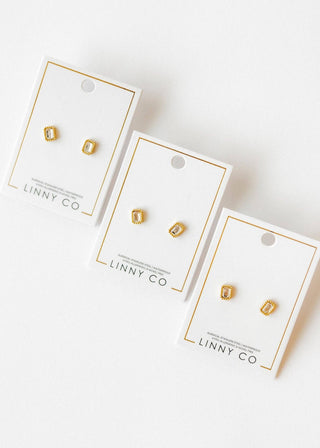 Three pairs of gold earrings on LINNY CO branded cards against a white background
