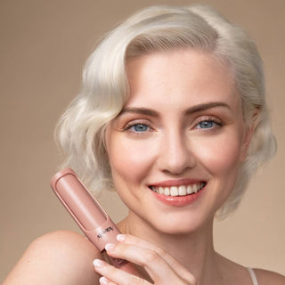 Woman holding a pink hair straightener against a beige background