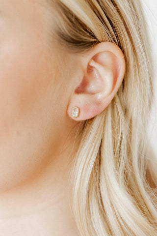 Close-up of an ear wearing a diamond earring with blonde hair.