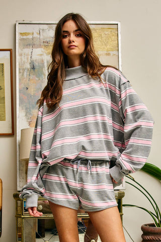 Woman wearing a gray and pink striped sweater and shorts in a room with a painting on the wall.