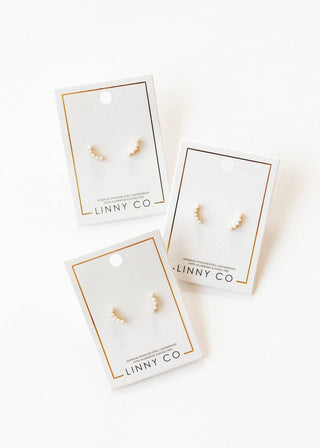Three pairs of gold earrings on LINNY CO branded cards against a white background