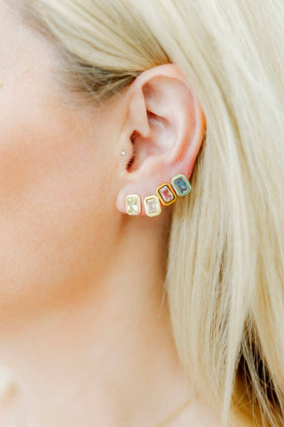 Close-up of an ear wearing colorful stud earrings with blonde hair.