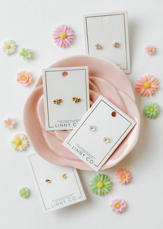 Gold bee earrings on LINNY CO cards with decorative flowers on a white background