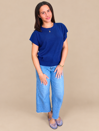 A woman modeling a royal blue short-sleeve t-shirt and light wash wide-leg jeans against a solid beige studio background.