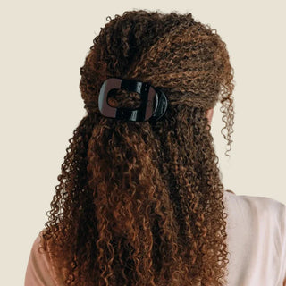 Person with long, curly hair wearing a black hair clip on a white background