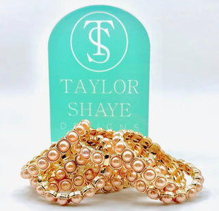 Gold and pink beaded bracelets on a display card with 'Taylor Shaye Designs' branding.