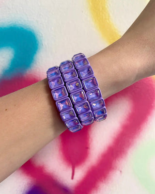 Purple beaded bracelet on a wrist with a colorful background
