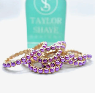Purple beaded bracelets on a white surface with a 'Taylor Shave' product in the background.