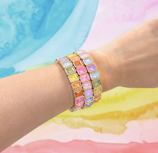 Multicolored gemstone bracelet on a wrist with a pastel background