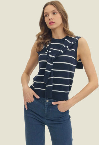 Woman wearing a navy and white striped sleeveless top with blue jeans against a plain background