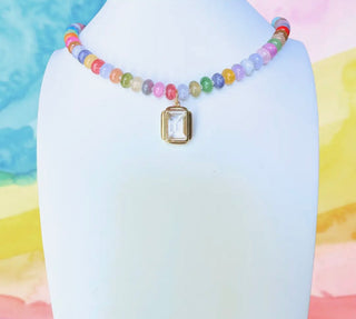 Colorful beaded necklace with a rectangular pendant on a white mannequin against a colorful watercolor background