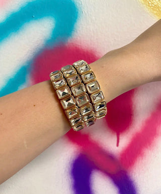 Gold bracelet on a wrist with a colorful tie-dye background