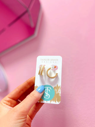 Hand holding a card with gold hoop earrings on a pink background