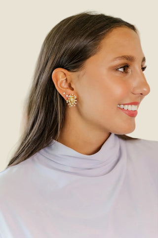 Woman wearing sparkling earrings with a solid cream background