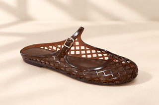 A single brown translucent jelly slip-on sandal with a grid pattern and a small buckle strap, shown on a warm beige background with soft shadows.