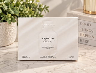 Michael Malul Vanilla+ Claire Eau de Parfum packaging box, displayed on a marble surface with a potted plant and decorative books in the background.
