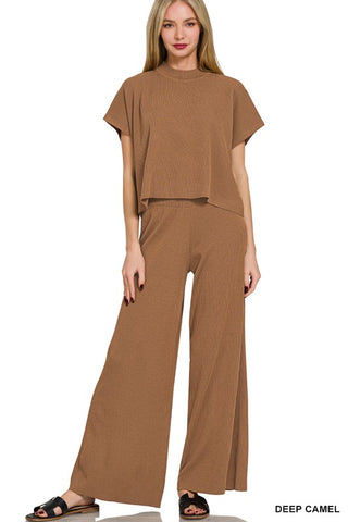 A woman modeling a matching two-piece set in deep camel brown, featuring a short-sleeve cropped knit top and wide-leg pants, shown against a plain white background.
