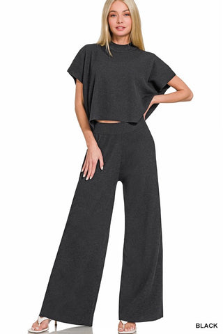 Woman wearing a black outfit with wide-leg pants and a crop top on a white background
