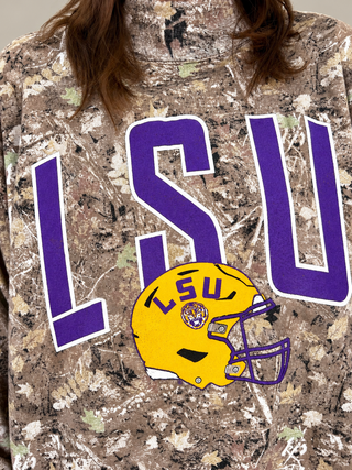 A close-up of a person wearing a camouflage sweatshirt with a large purple 'LSU' graphic and a yellow LSU football helmet graphic on the front.