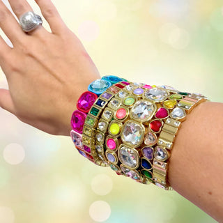 Hand wearing multiple colorful gemstone bracelets on a blurred background