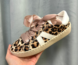 Leopard print sneaker with pink ribbons held against a gray background