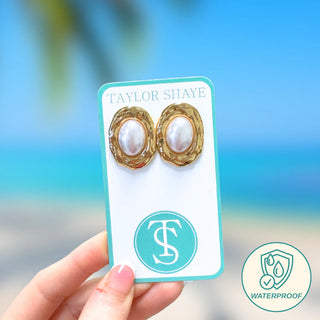 Gold and pearl earrings on a Taylor Shaye card with a blurred background