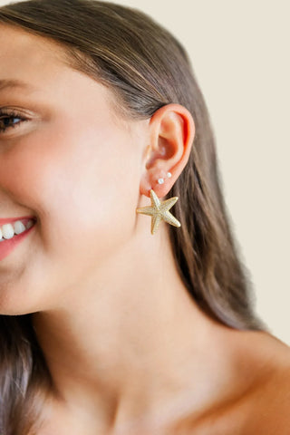 Close-up of a woman wearing a gold starfish earring with a blurred background