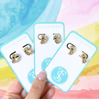 Taylor Shaye earrings on display with a hand holding the packaging against a colorful background
