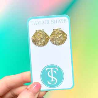 Gold shell-shaped earrings on a Taylor Shaye card against a colorful background