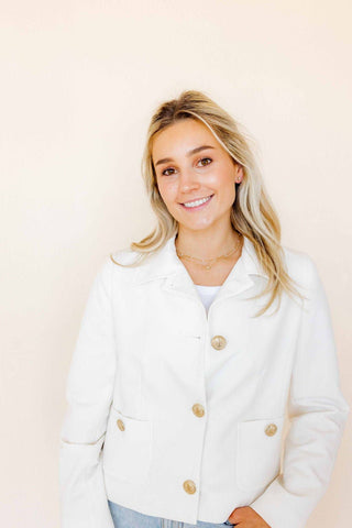 Woman wearing a white jacket with gold buttons against a plain background