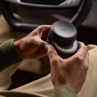A close-up of a person's hands holding a dark gray circular Euro Air personal air purifier inside a car interior.