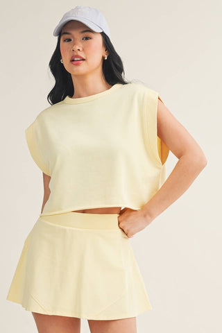 Woman wearing a light yellow outfit with a matching cap against a plain background