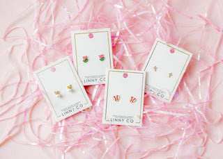 Set of earrings on LINNY CO cards with pink ribbons in the background