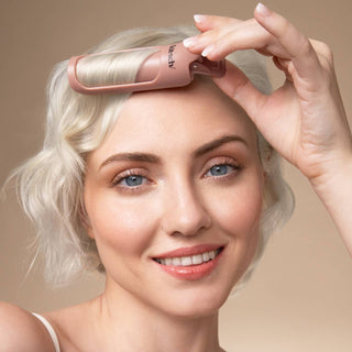 Woman using a pink hair styling tool on her head against a beige background
