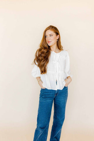 Woman wearing a white blouse and blue jeans against a beige background