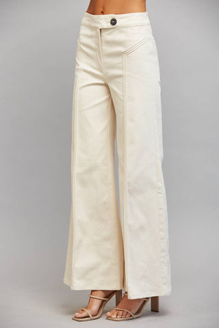 A model from the waist down wearing off-white wide-leg cropped pants and beige strappy high-heeled sandals, standing against a neutral gray studio background.