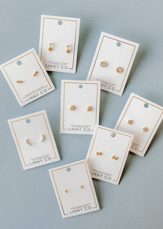 Gold earrings on LINNY CO branded cards against a light gray background