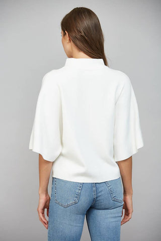 A woman viewed from the back wearing a white short-sleeve mock-neck top and light blue jeans against a plain gray studio background.