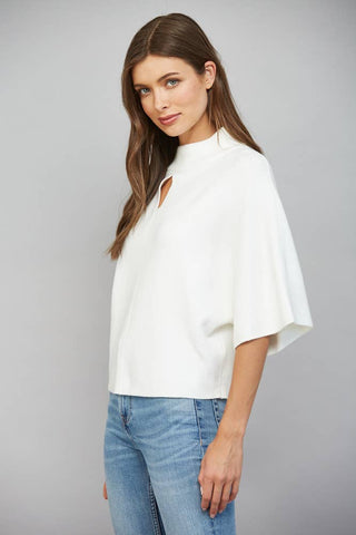 A woman modeling a white short-sleeve top with a mock neck and a keyhole cutout at the collar, paired with blue jeans, against a solid gray studio background.