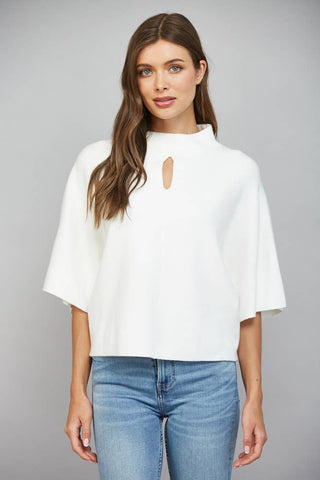 A woman modeling a white short-sleeve mock-neck top with a keyhole cutout at the collar, paired with blue jeans, against a solid gray studio background.
