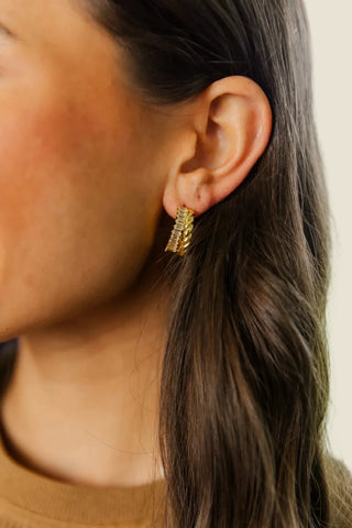 Close-up of a person wearing gold hoop earrings with a blurred background