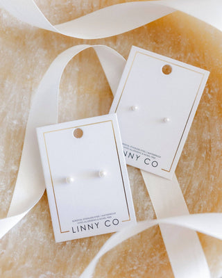 Pair of earrings on LINNY CO branded cards with ribbons on a beige background