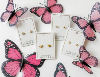 Butterfly-themed earrings on LINNY CO cards with pink butterflies around.