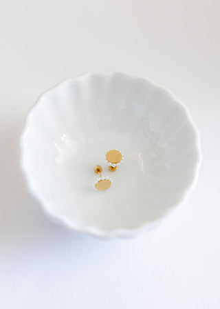 Pair of gold and pearl stud earrings on a white dish.