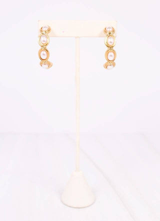Gold earrings on a white stand with a white background