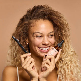 Woman holding a Kiehl's skincare product and brush against a beige background