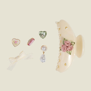 Set of decorative items including a shell with floral design, heart-shaped object, and small jewelry pieces on a light background.