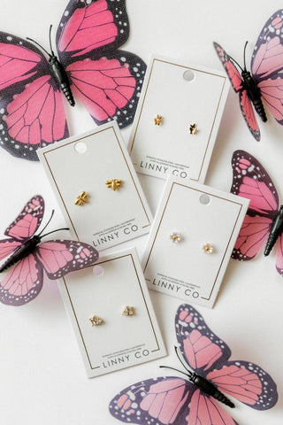 Gold earrings on LINNY CO cards with pink butterfly decorations on a white background