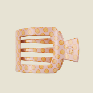 A single hair claw clip with a light pink background and a repeating yellow sunburst pattern, shown on a solid light beige background.